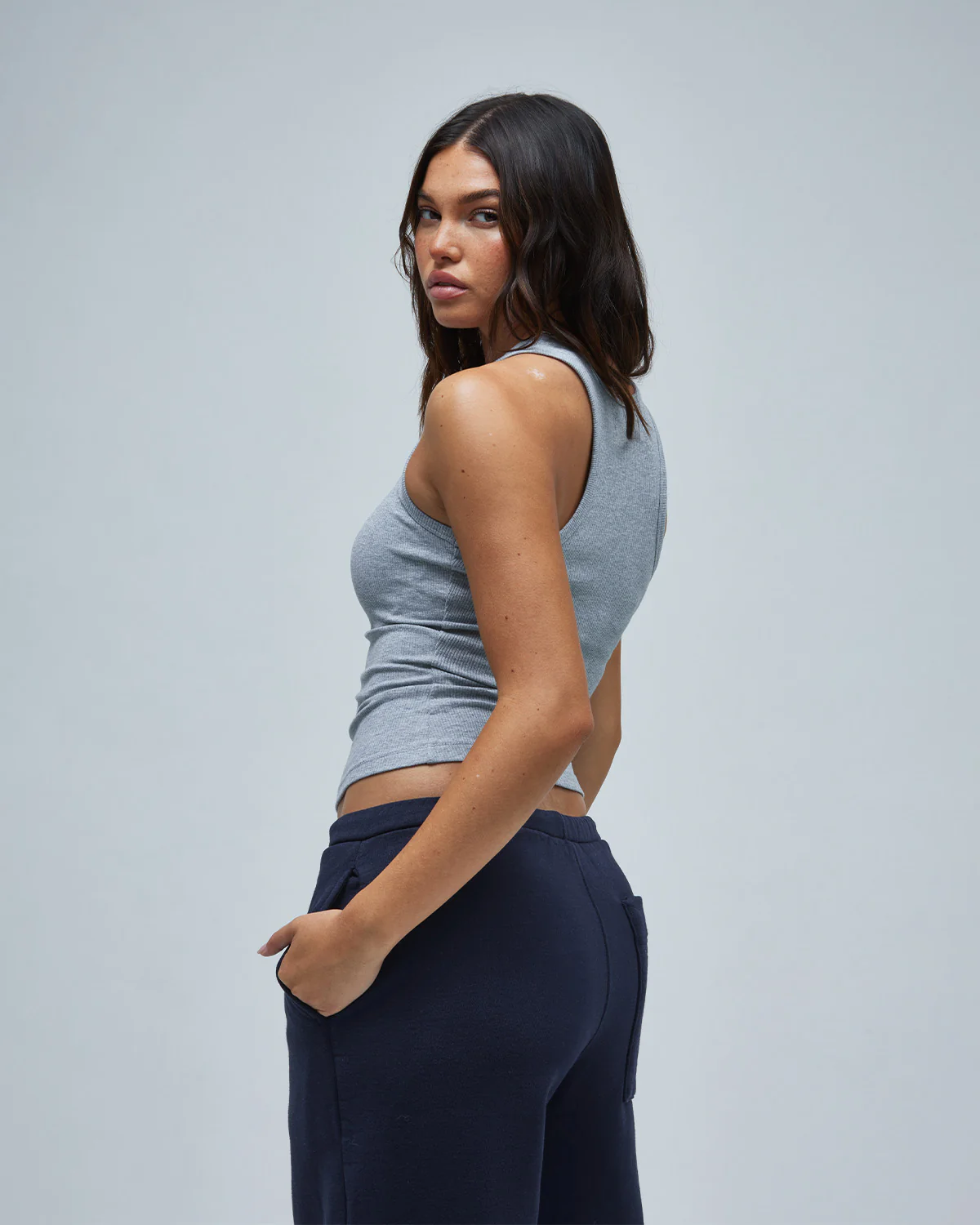 A woman wearing blue track pants & a gray tank top