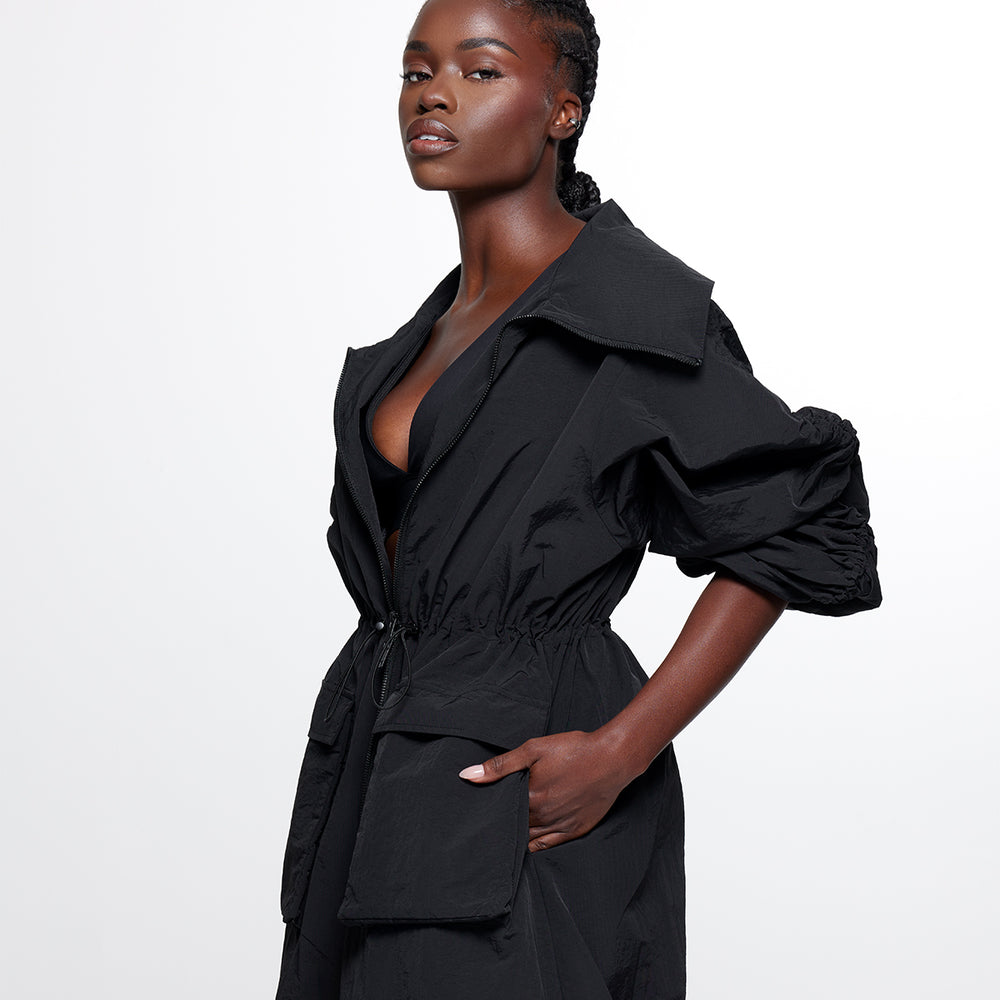 
                  
                    black mid-length nylon trench jacket. fold over collar, two-way zip closure, bungee cinch at the waist, hem, two front pockets, two side seam pockets.
                  
                