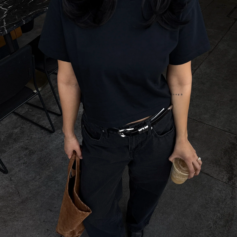 A woman in a baby tee shirt and black pants holding coffee