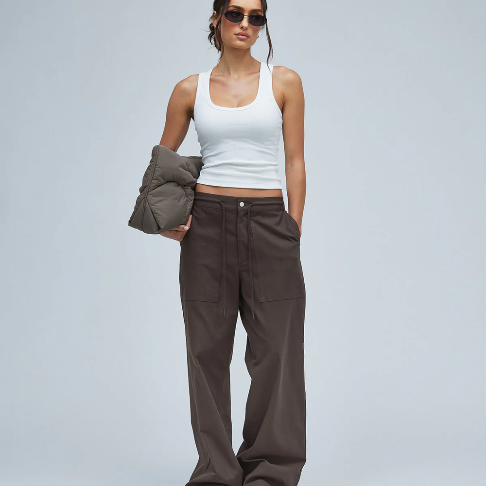 Woman wearing brown pants and white tee holding a brown puffer bag