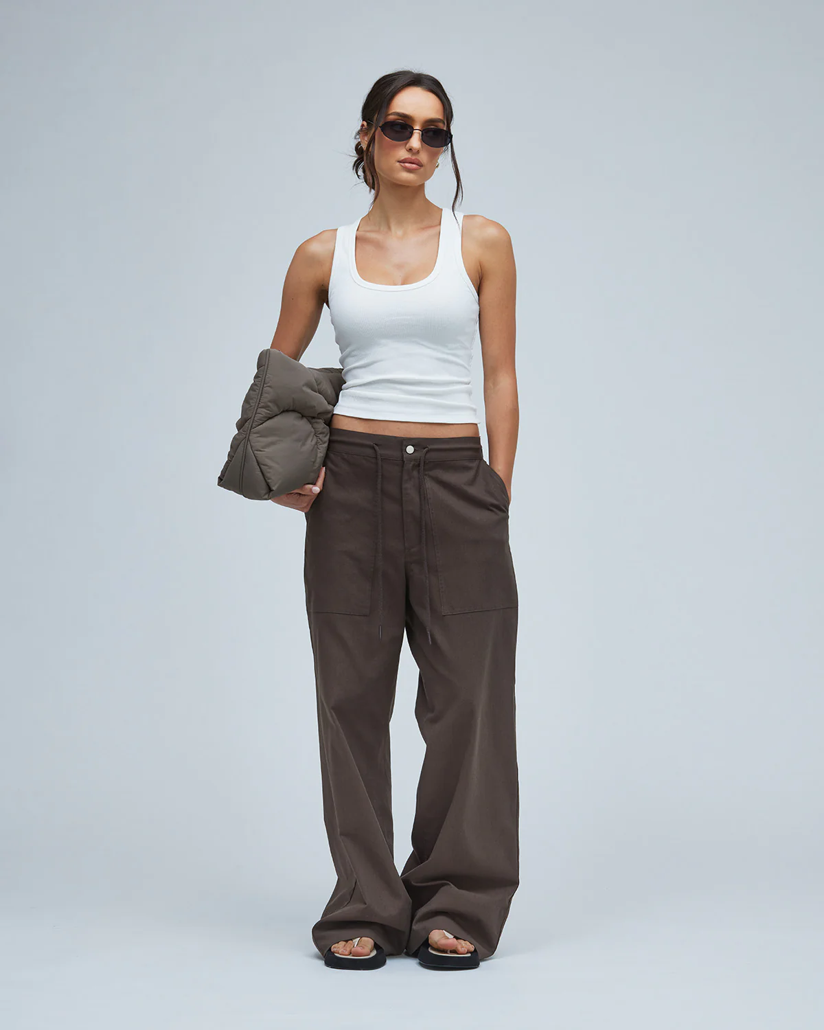 Woman wearing brown pants and white tee holding a brown puffer bag