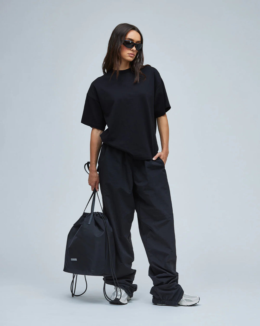 A model wearing black-colored women's nylon track pants & a T-shirt while holding a black bag